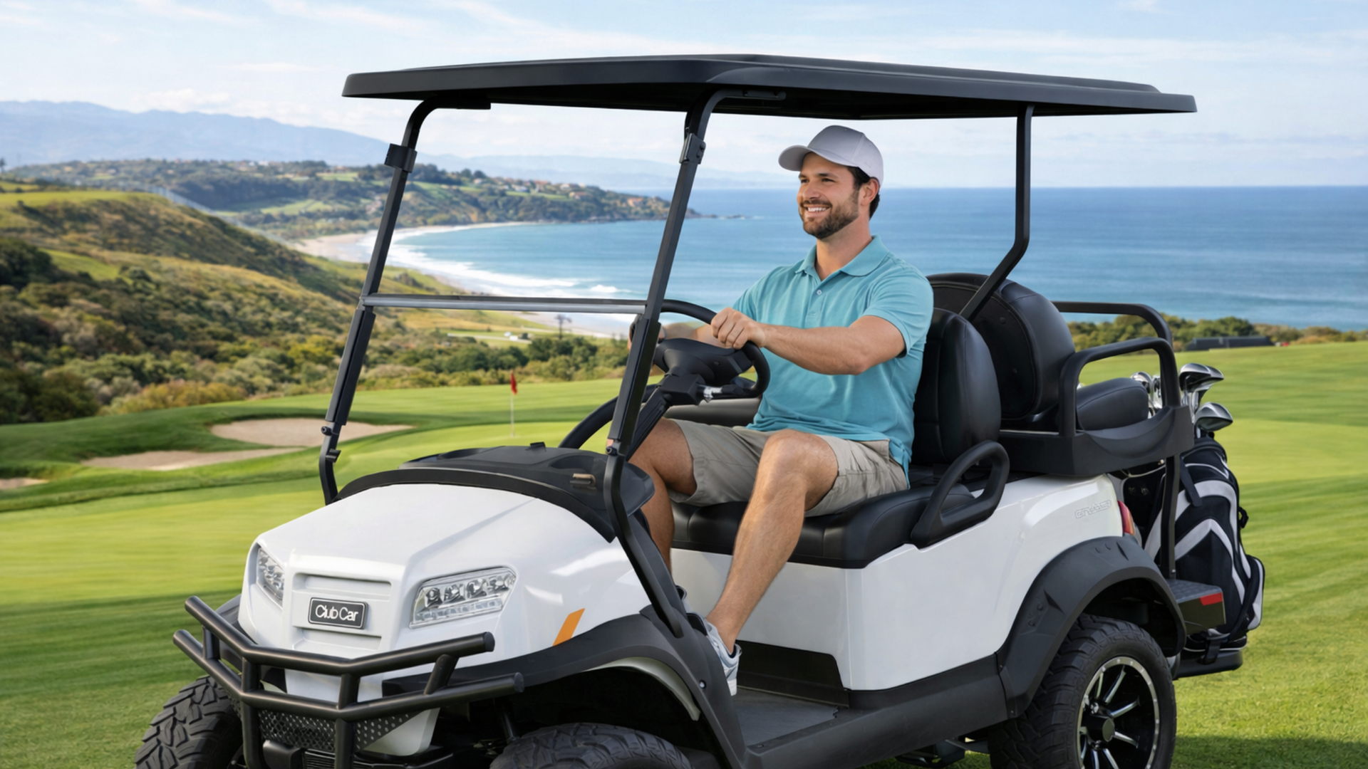 Smiling golfer driving white golf cart on coastal course with ocean view, rolling fairways, and golf clubs on the back rack.