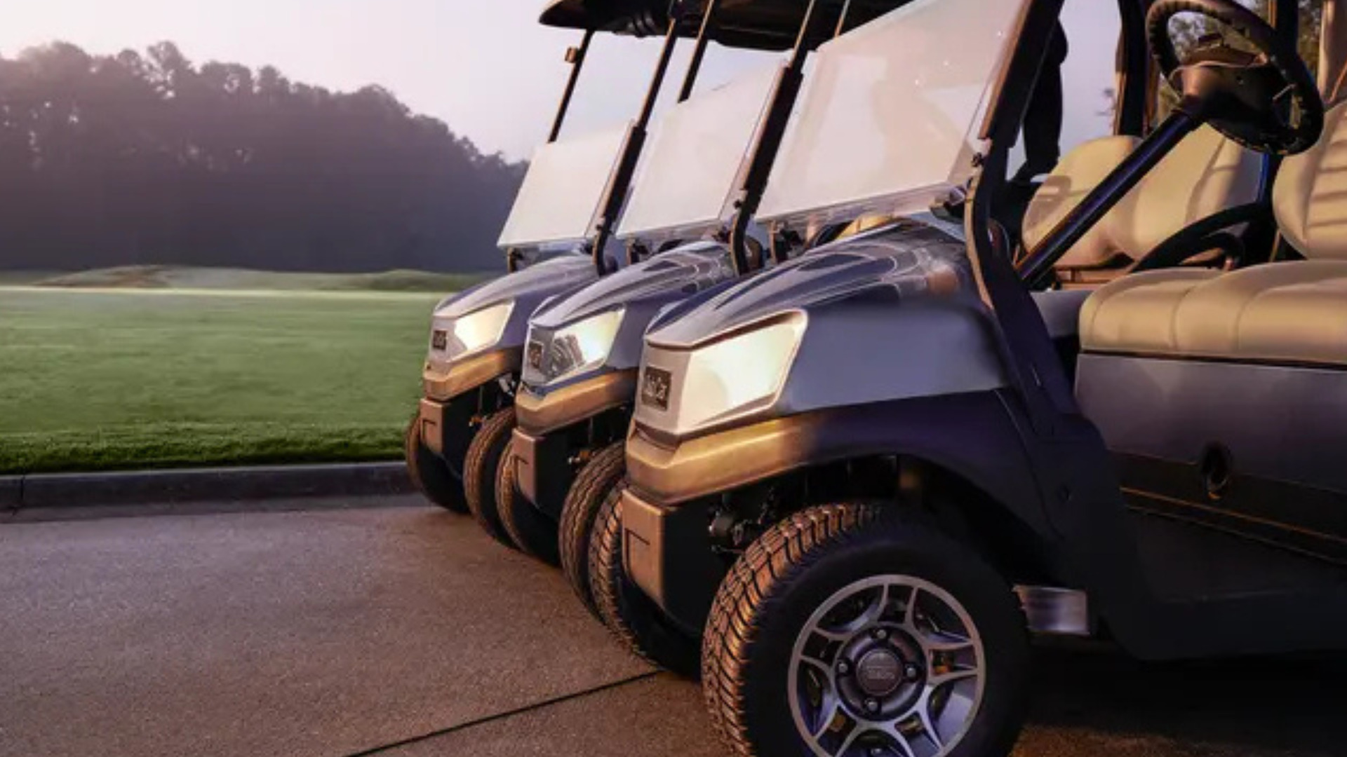 Row of golf carts in Phoenix lined up near a course with windshields, headlights, and early morning lighting.
