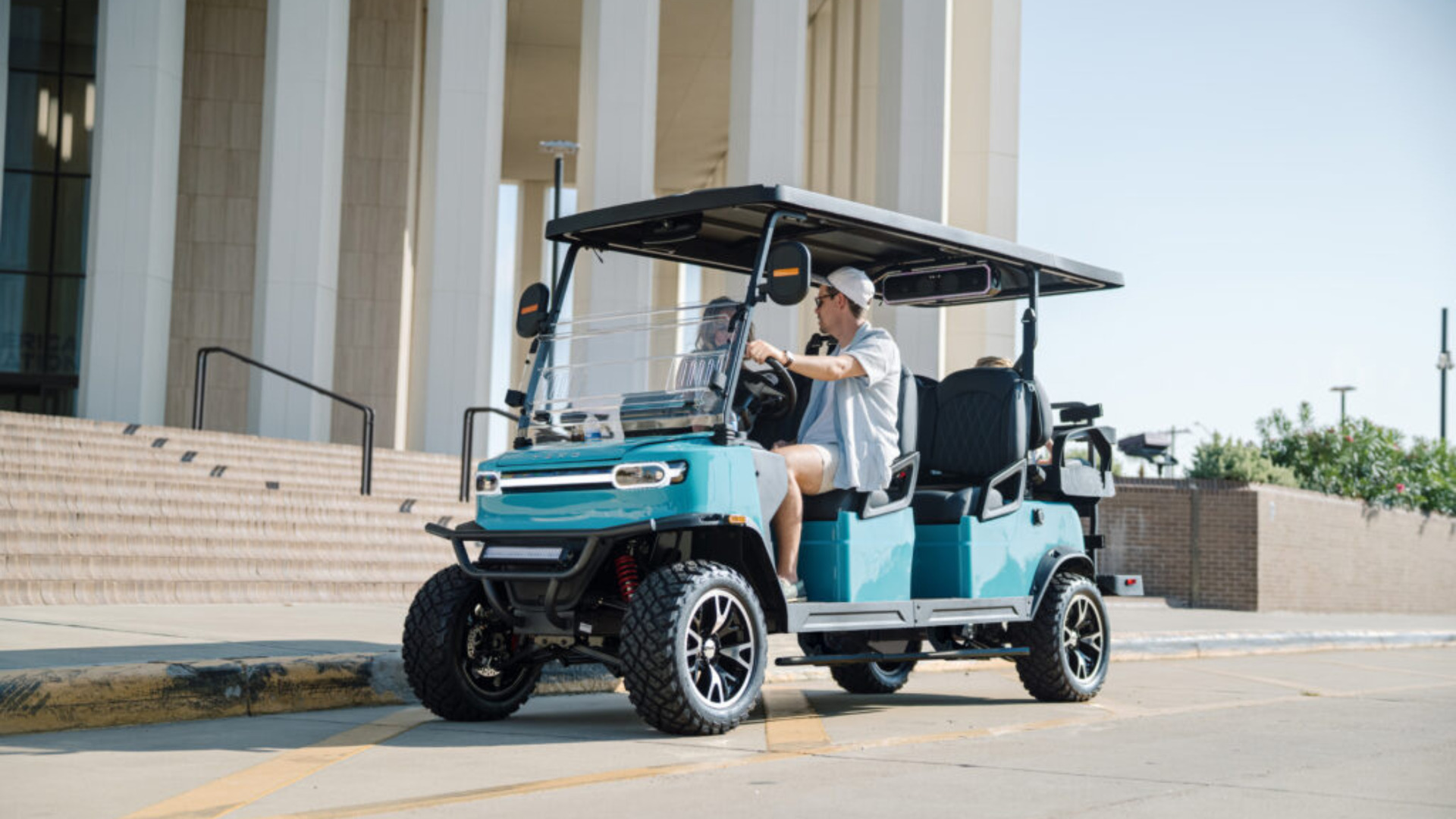 Blue lifted golf cart in San Diego carrying passengers near a building with canopy roof and off-road tires.