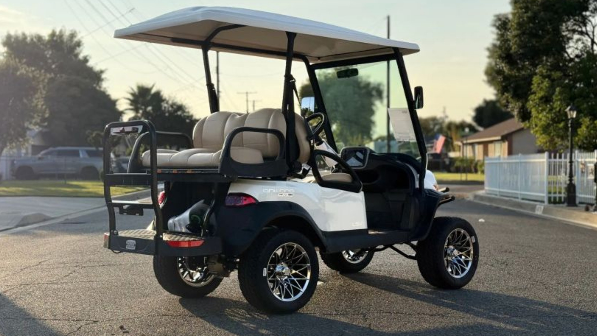 White Club Car Onward lifted golf cart with rear seat on neighborhood street.