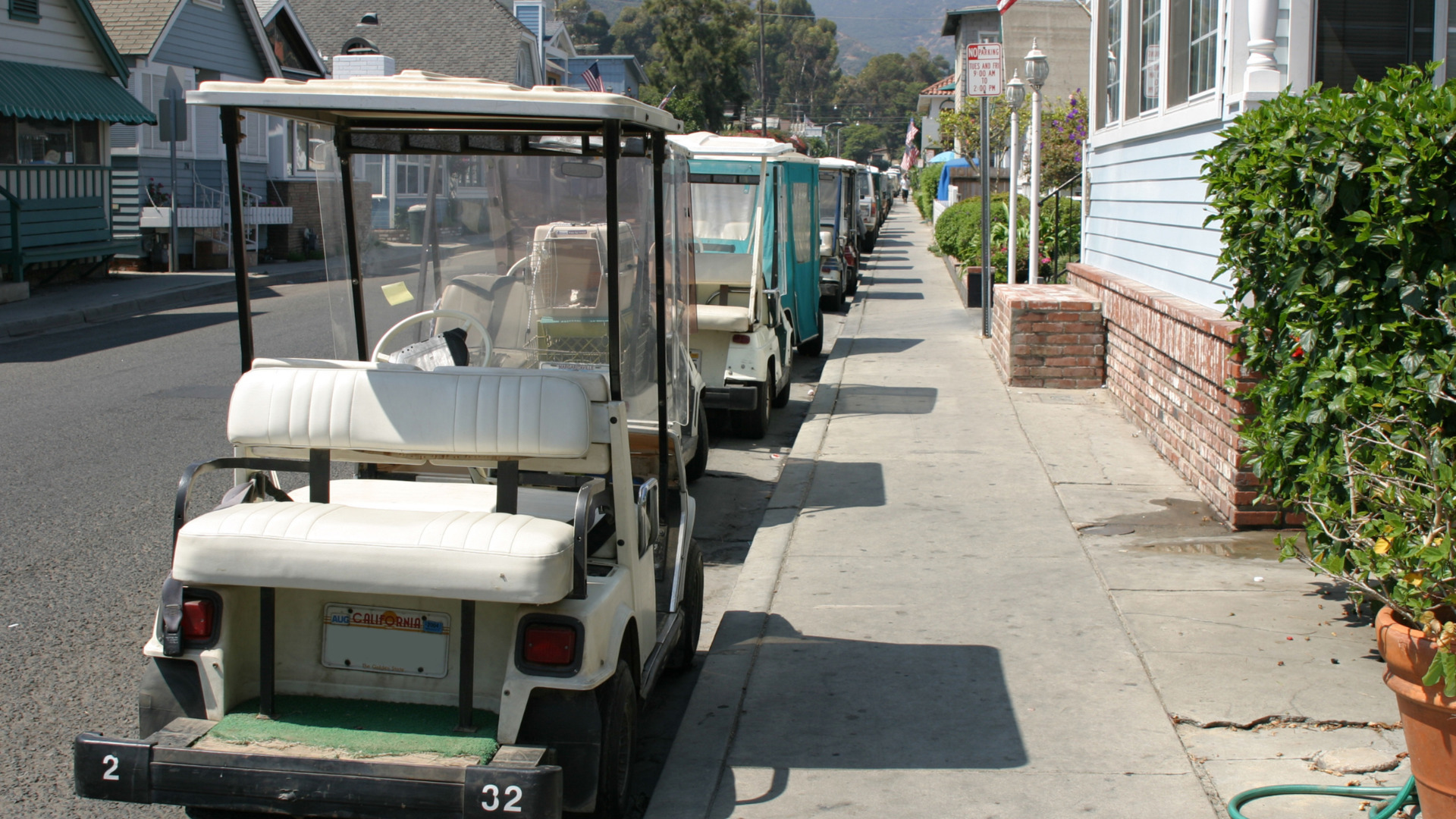 White golf cart parked along a residential street with multiple golf carts lined up behind it.