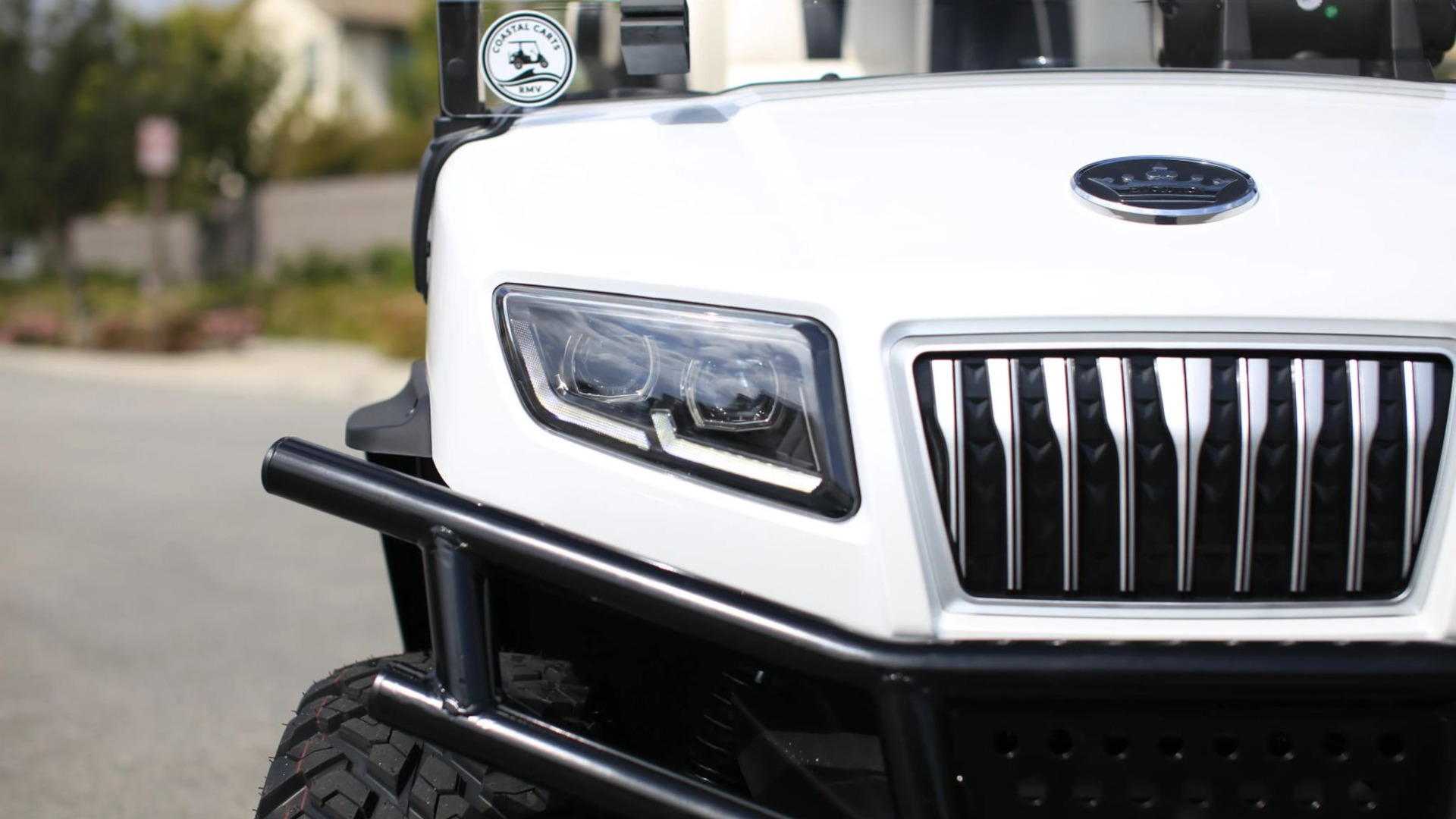 Close-up of a white golf cart front end with headlight, grille, and bumper guard.