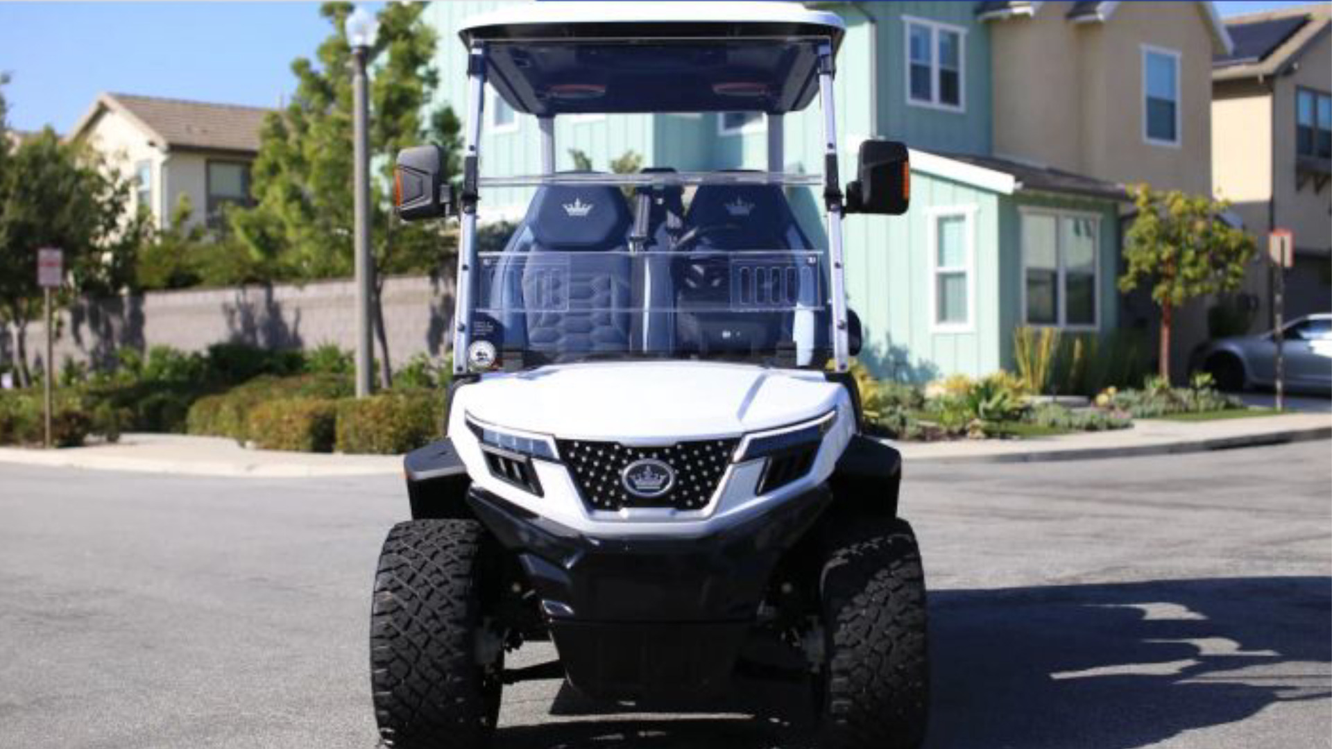 Front view of a white lifted golf cart parked on a residential street.