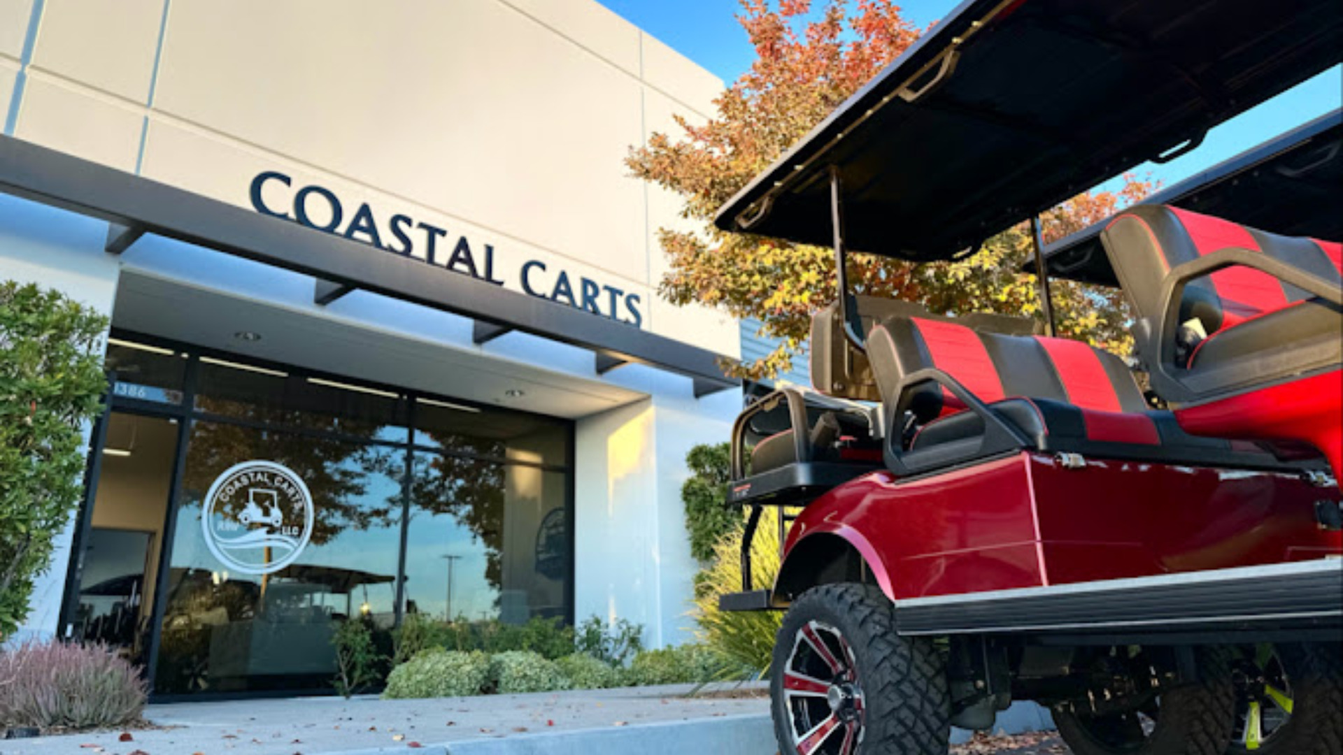 Red lifted golf cart parked outside the Coastal Carts storefront entrance.