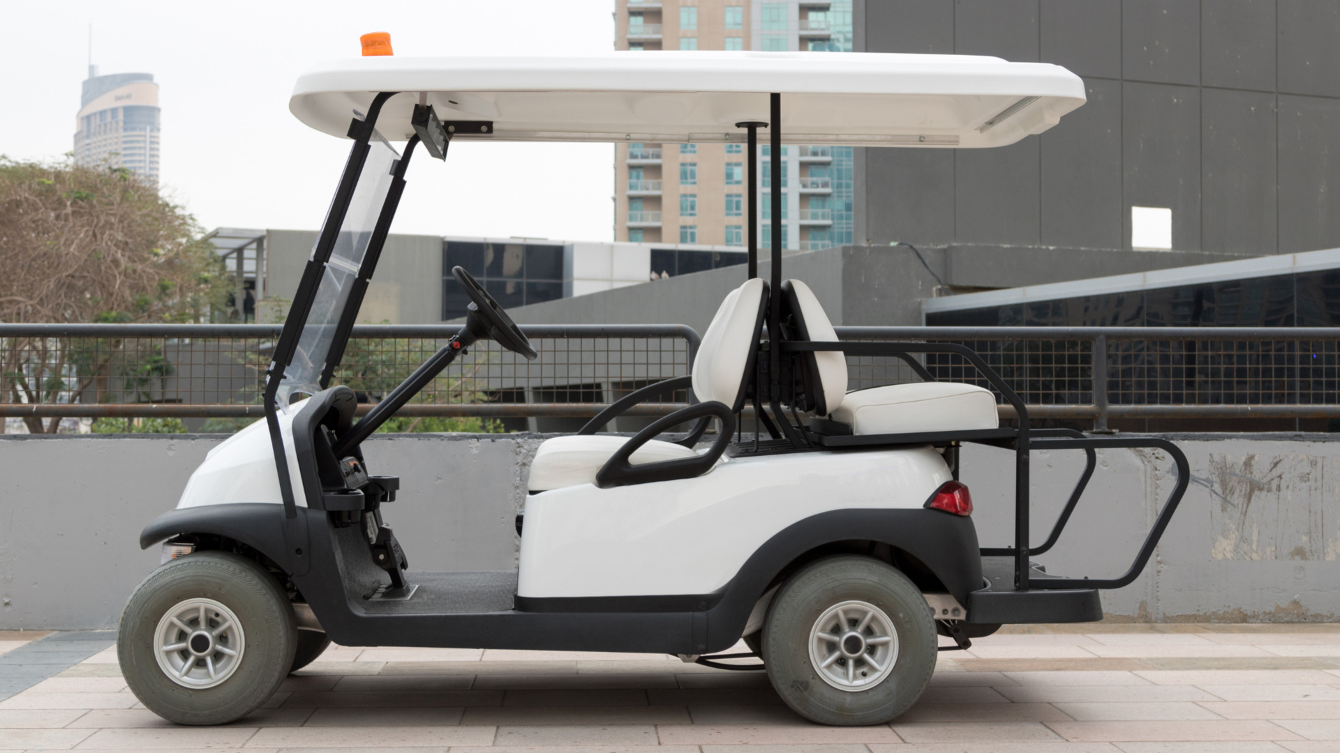 White golf cart shown in side view on an urban rooftop parking area with city buildings behind it.