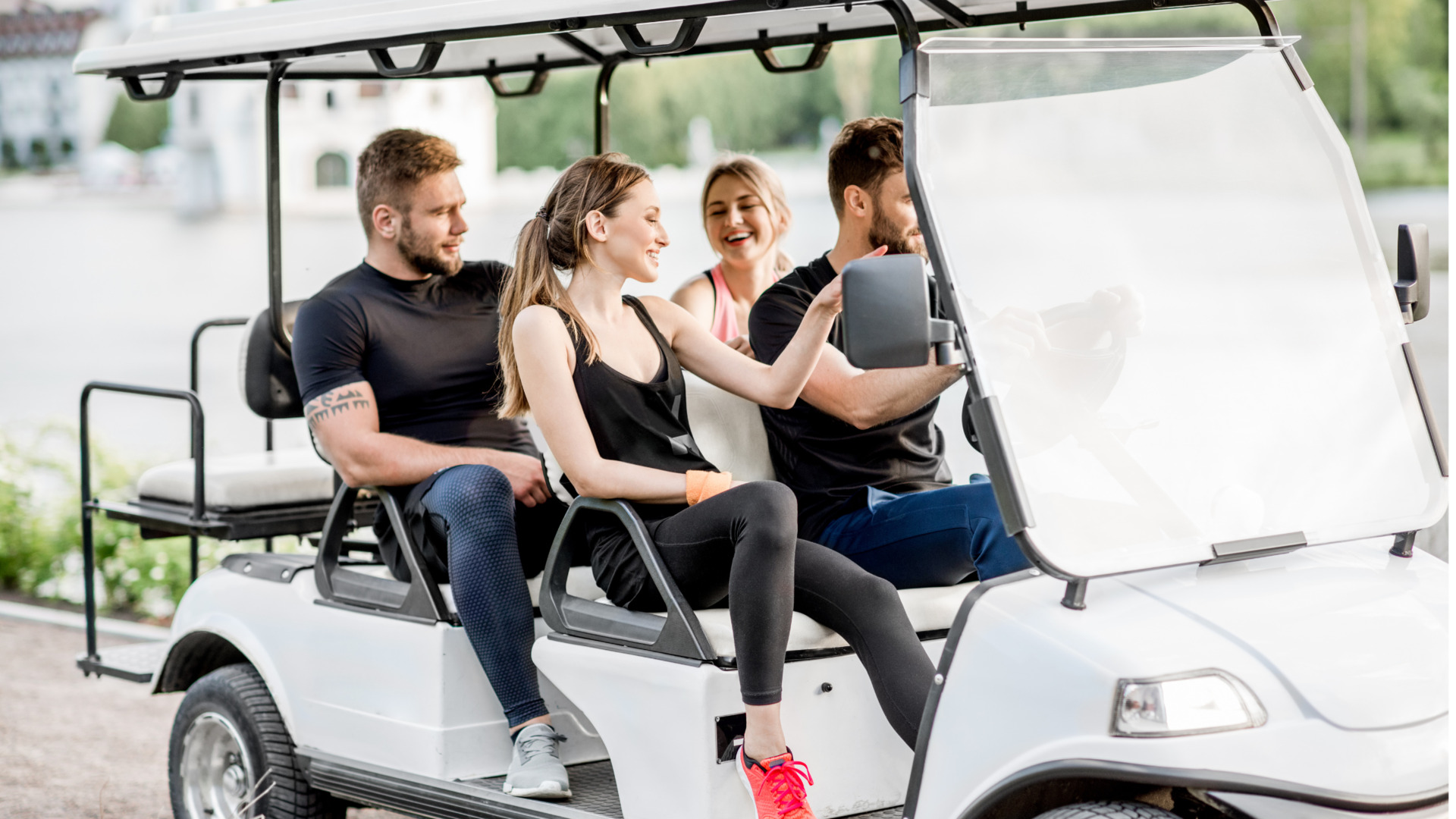 Four people riding in a white golf cart outdoors in casual athletic wear.