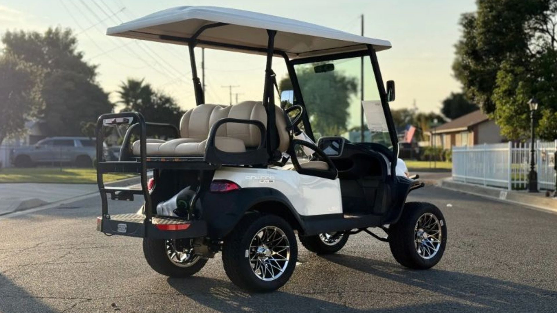White Club Car Onward lifted golf cart with rear seat on neighborhood street.