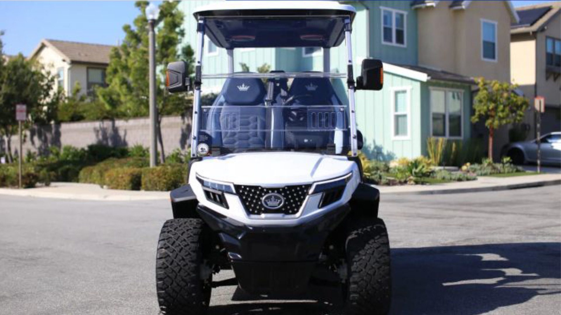 Front view of a white lifted golf cart parked on a residential street.