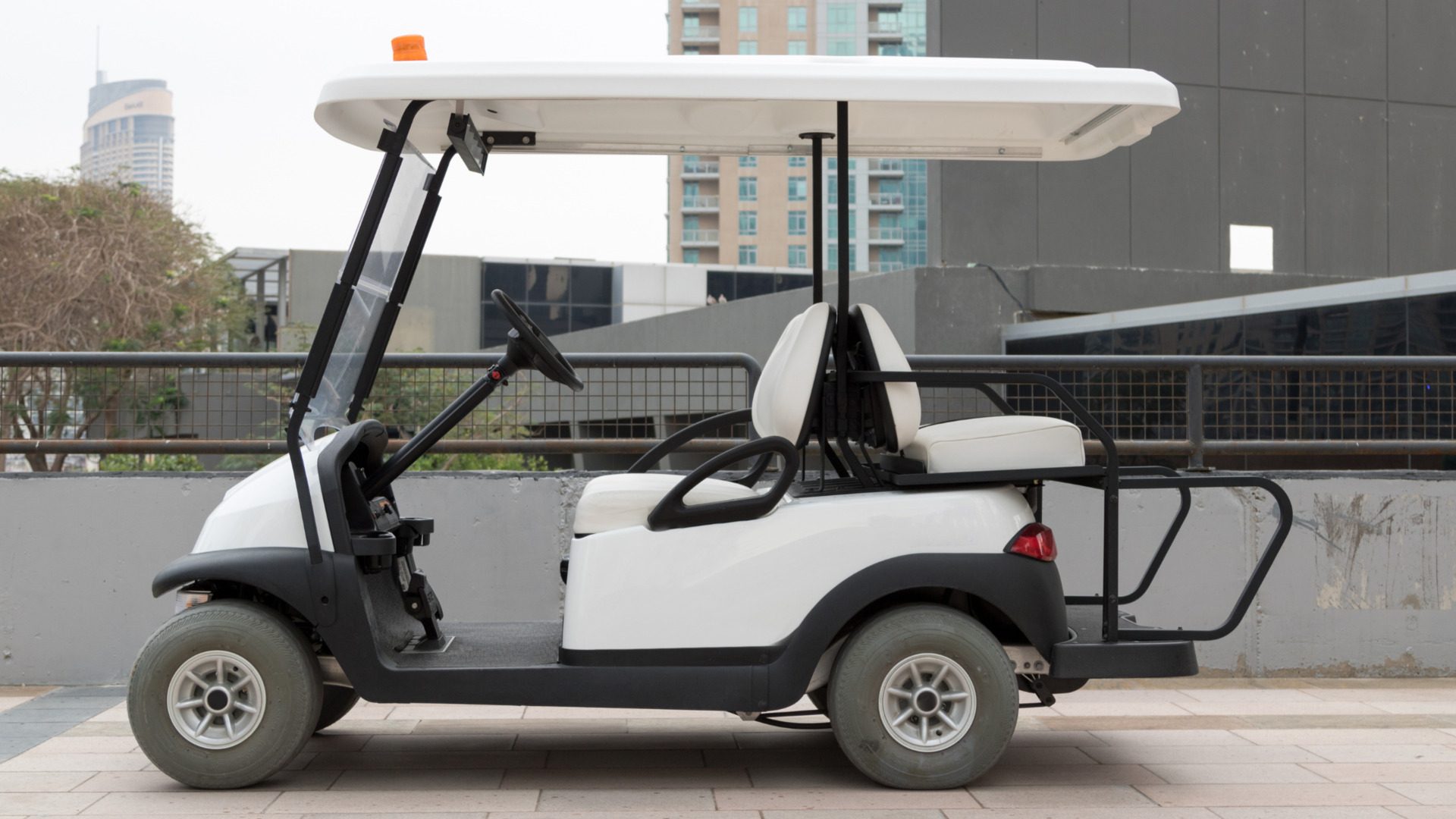 White golf cart shown in side view on an urban rooftop parking area with city buildings behind it.