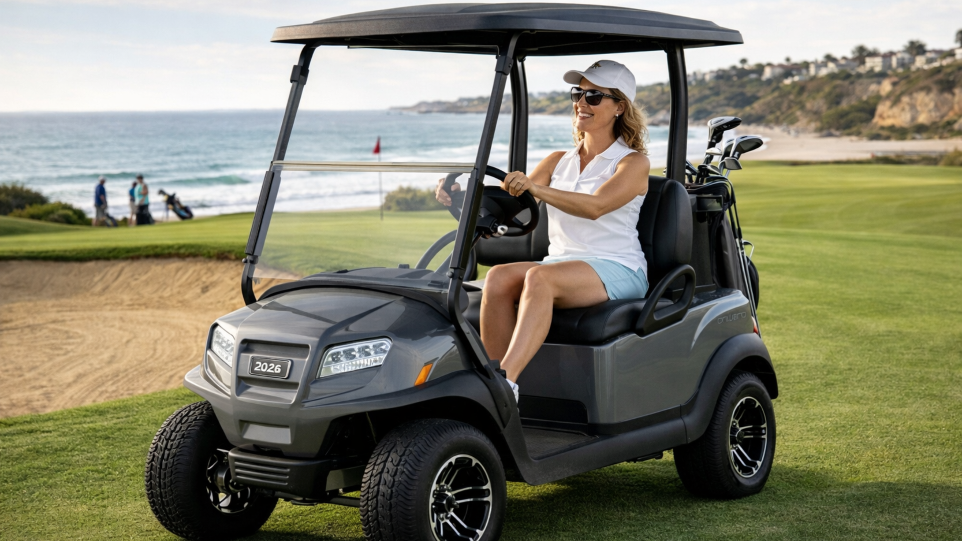 Woman driving gray street legal golf cart on a seaside fairway near a sand bunker with ocean backdrop and golf clubs mounted behind the seat.